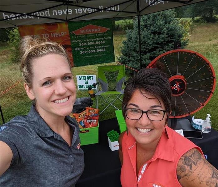 Two SERVPRO ladies standing in front of table display and tent